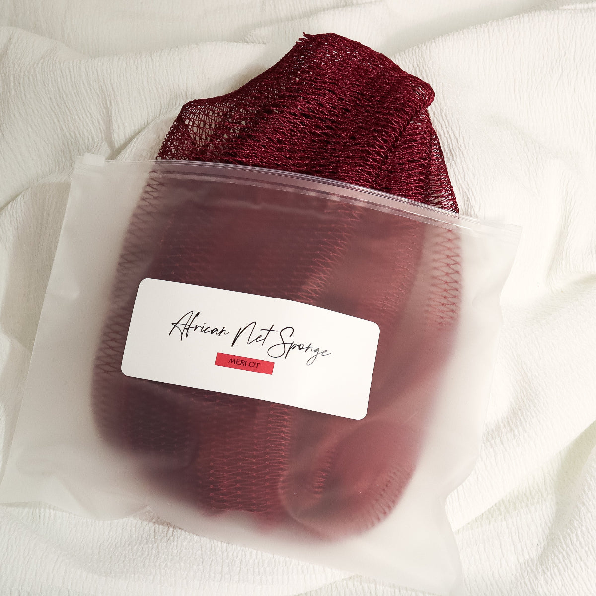 Wine red African net sponge in a clear zip bag with a product label on a white background