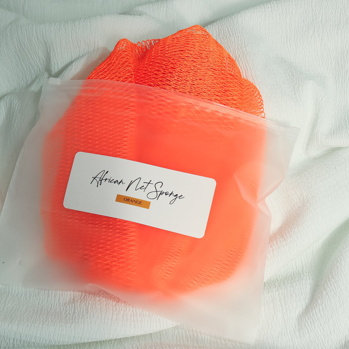 Orange African net sponge in a clear zip bag with a product label on a white background