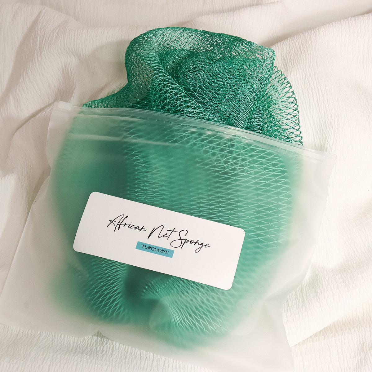 Turquoise African net sponge in a clear zip bag with a product label on a white background