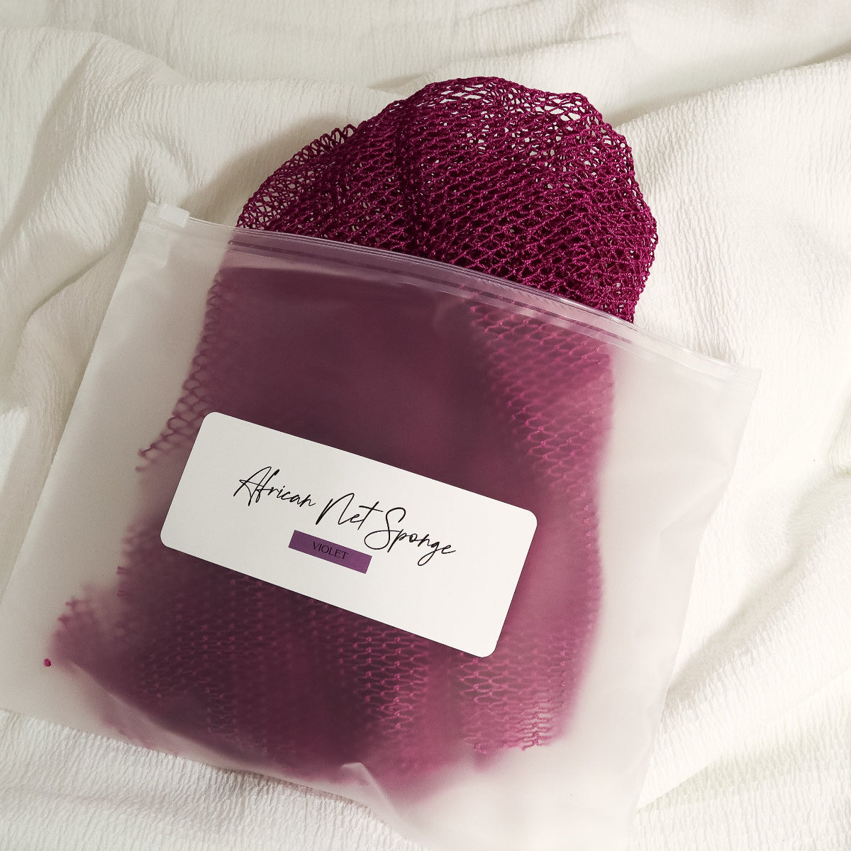Violet African net sponge in a clear zip bag with a product label on a white background